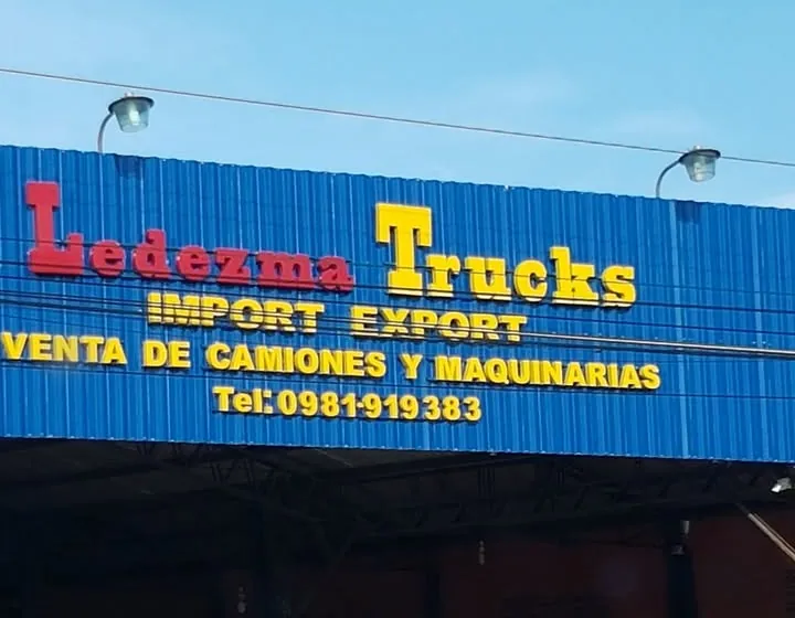 Frente del galpón de chapa azul con el cartel Ledezma Trucks, Import Export, venta de camiones y maquinarias