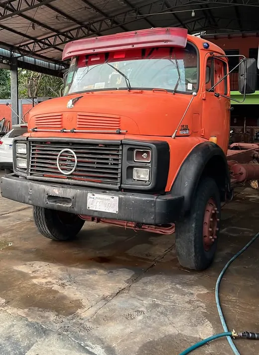 Camión Mercedes-Benz naranja de cabina alta, estacionado bajo el galpón