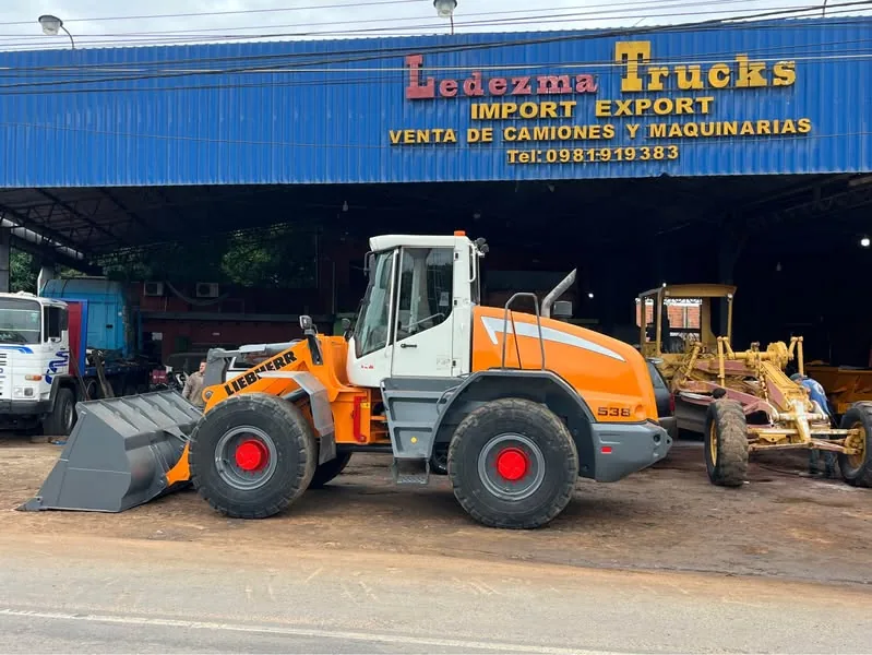 Pala cargadora Liebherr y una motoniveladora frente al galpón con el cartel de Ledezma Trucks