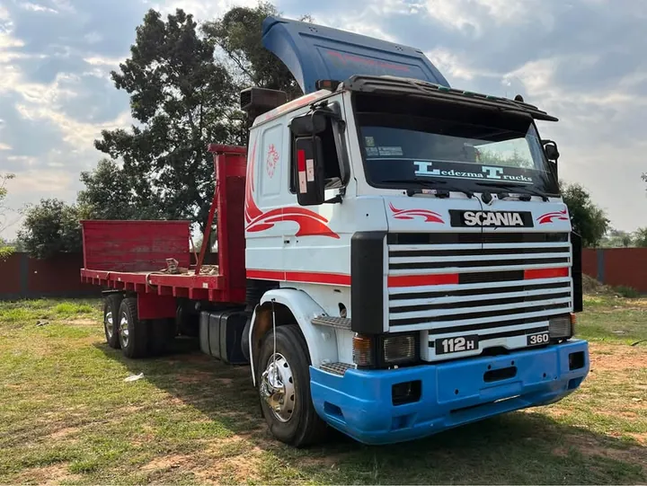 Camión Scania 112H blanco con franjas rojas y azules, rotulado Ledezma Trucks, con plataforma roja